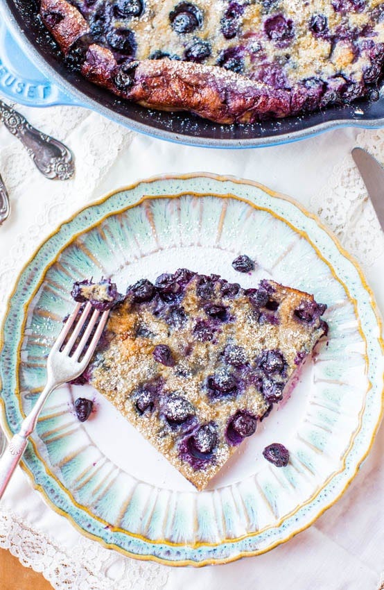 Blueberry Dutch Baby Pancake - Easy Recipe at averiecooks.com A slice of a blueberry dutch baby pancake in skillet next to slice on a plate.