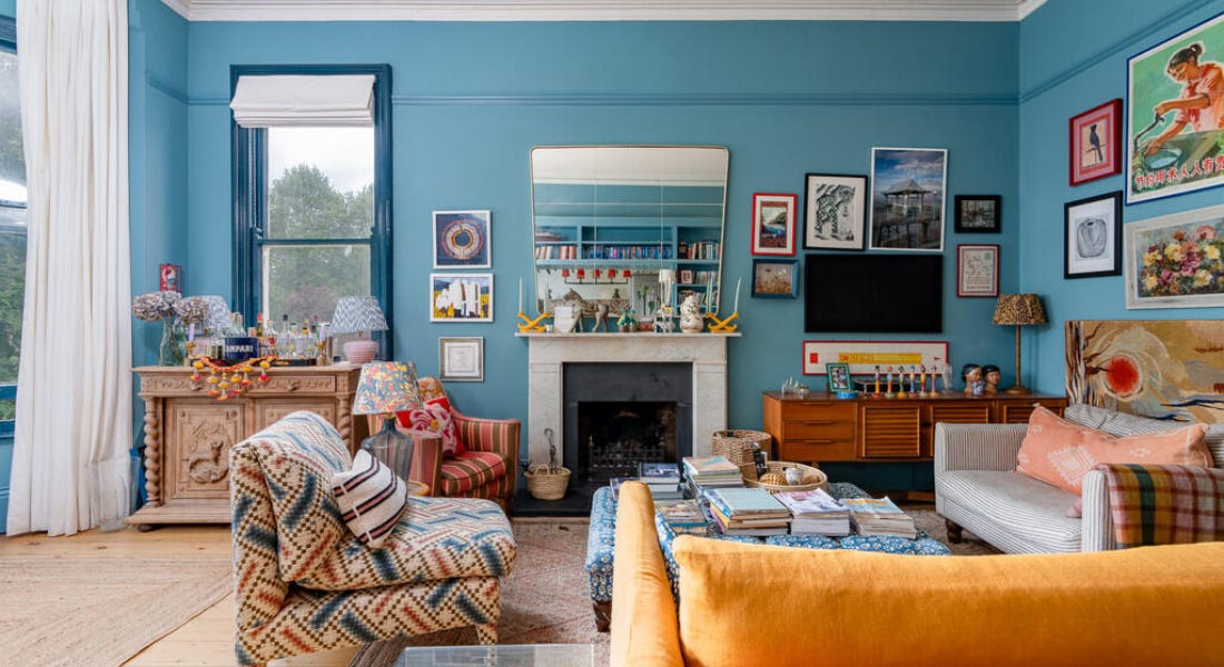 A blue living room with colourful couches, artworks, and a fireplace