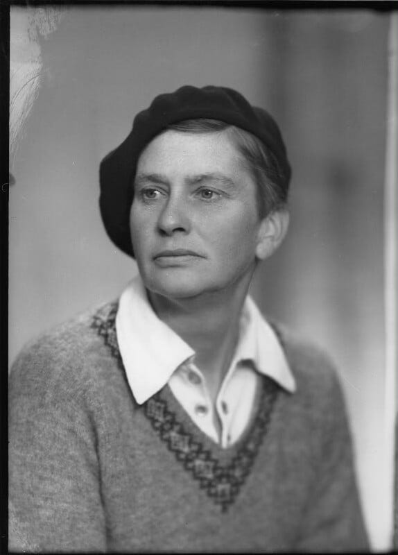 A striking light-skinned woman in her early forties (Lady Eve Balfour) wears a beret tilted to one side, an open-necked shirt and a fairisle jumper. The expression on her face is open but firm