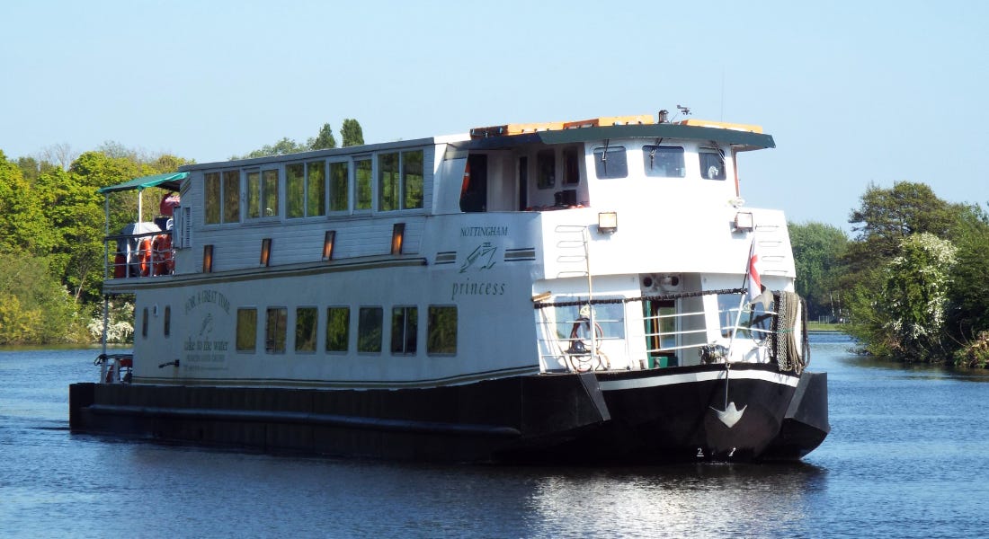 A white boar with windows on a river with greenery around it
