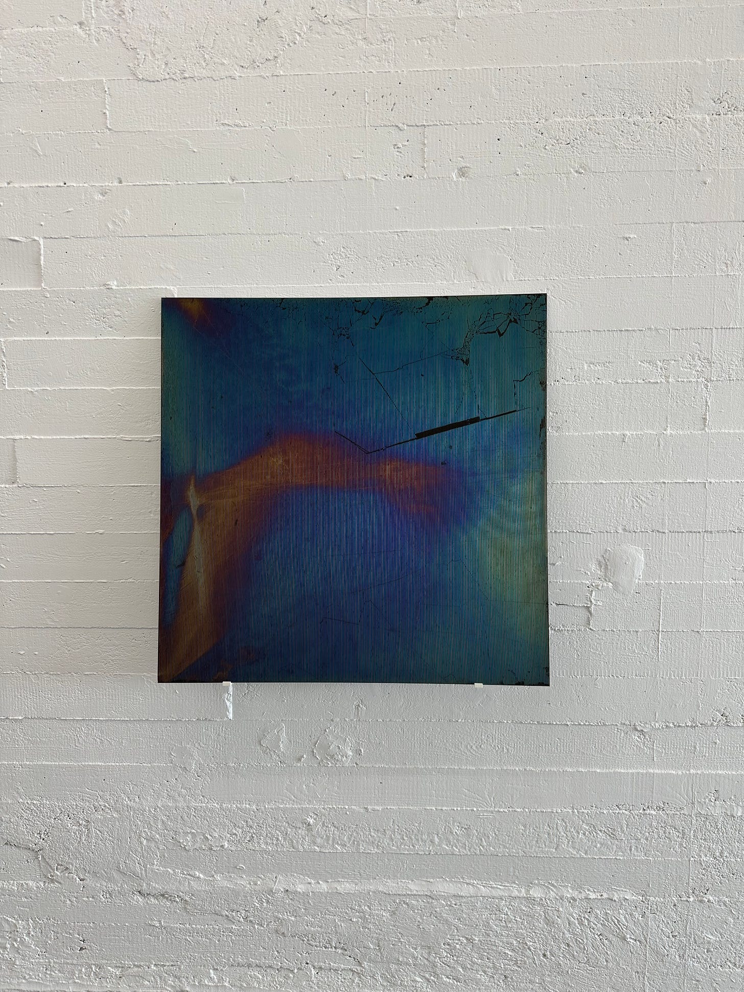 An iridescent dark panel that appears to be creaked. That is deliberate. Against the white wall, this panel shimmers as you go past. This untitled work is by Ann Veronica Janssens. She is an artist who explores reflections, luminosity and transparency.