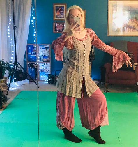 Two mirror-selfies on the green screen floor: a drab brown and olive ratty hunting outfit and a pretty-in-pink-and-sand pants and tunic outfit. And a pro shot of my She-Wolf fur and feathers wild-woman outfit in a dynamic, claw-handed pose with leg poised to kick and gaze aimed and fixed.