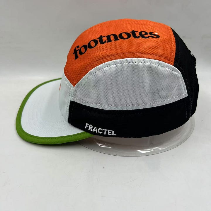 Images of the Footnotes Fractel hat including the orange logo on the front panel and underneath the brim. The newsletter's name is typed on the top of the hat and a green stripe accents the brim.