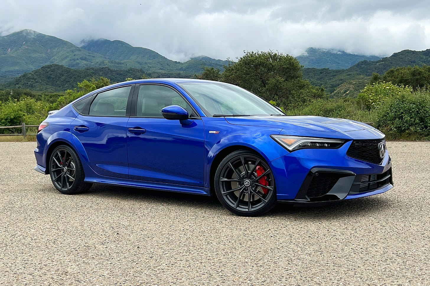 A blue 2024 Acura Integra Type S parked near mountains on a cloudy day.