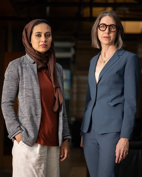 A woman in a head scarf and a woman in a suit with round glasses.