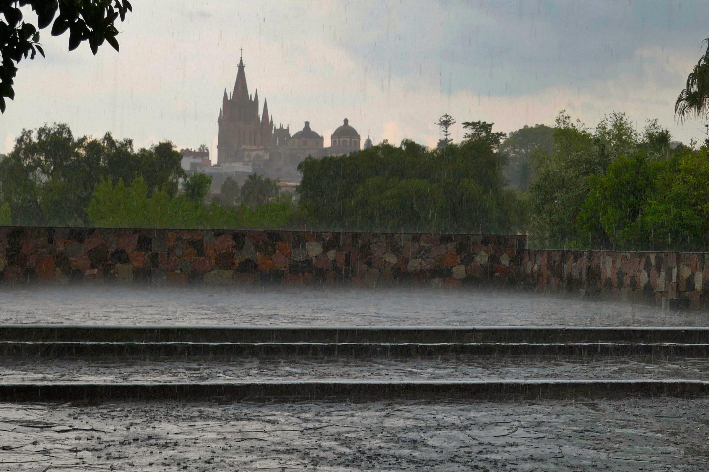 View of a cathedral in the distance with a courtyard in the forefron with the heavy rain splashing on the grey stone steps