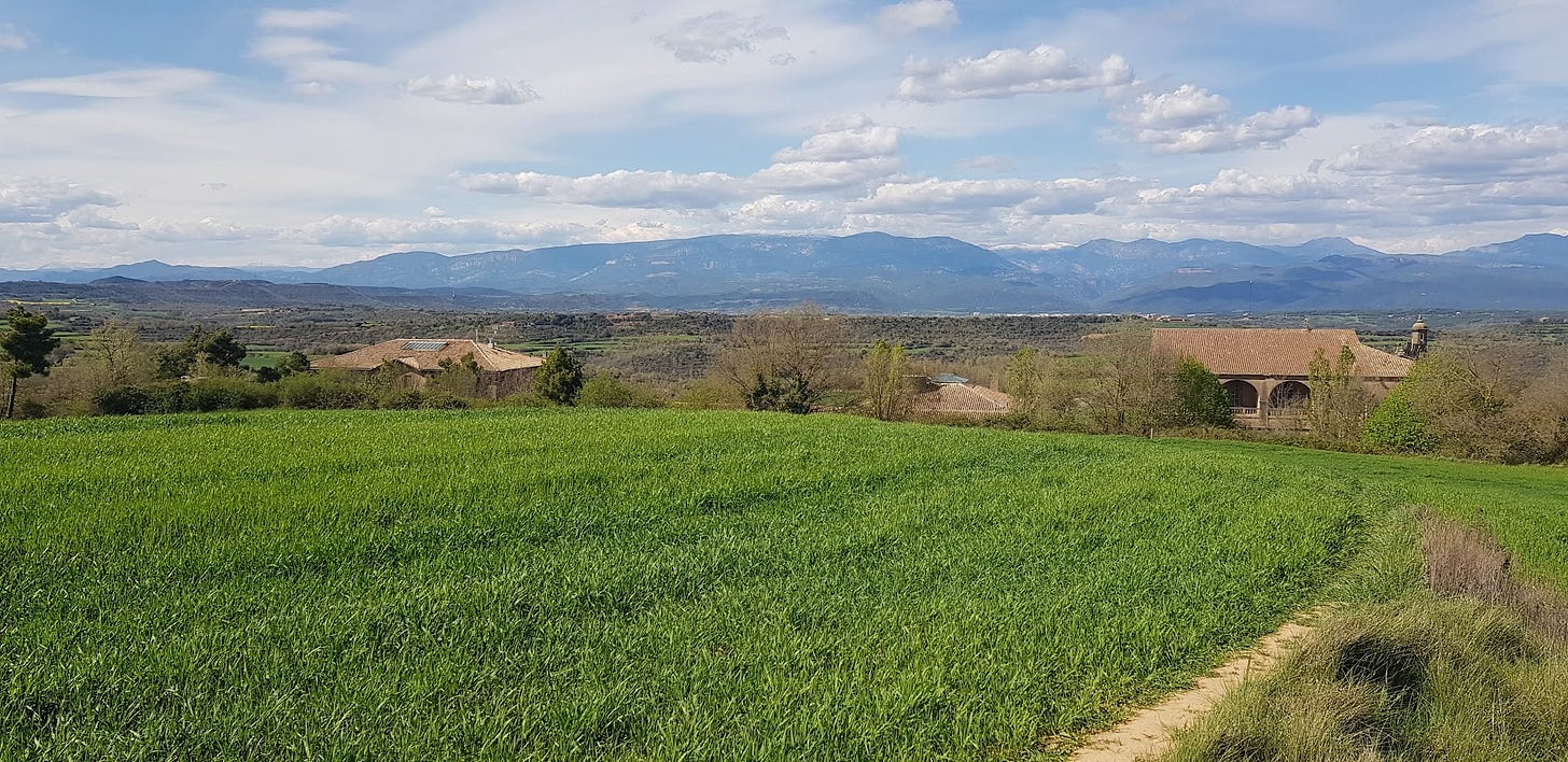 Landscape shot from the top of a Spanish mountain of the green fields and hills all around under a blue cloudy sky