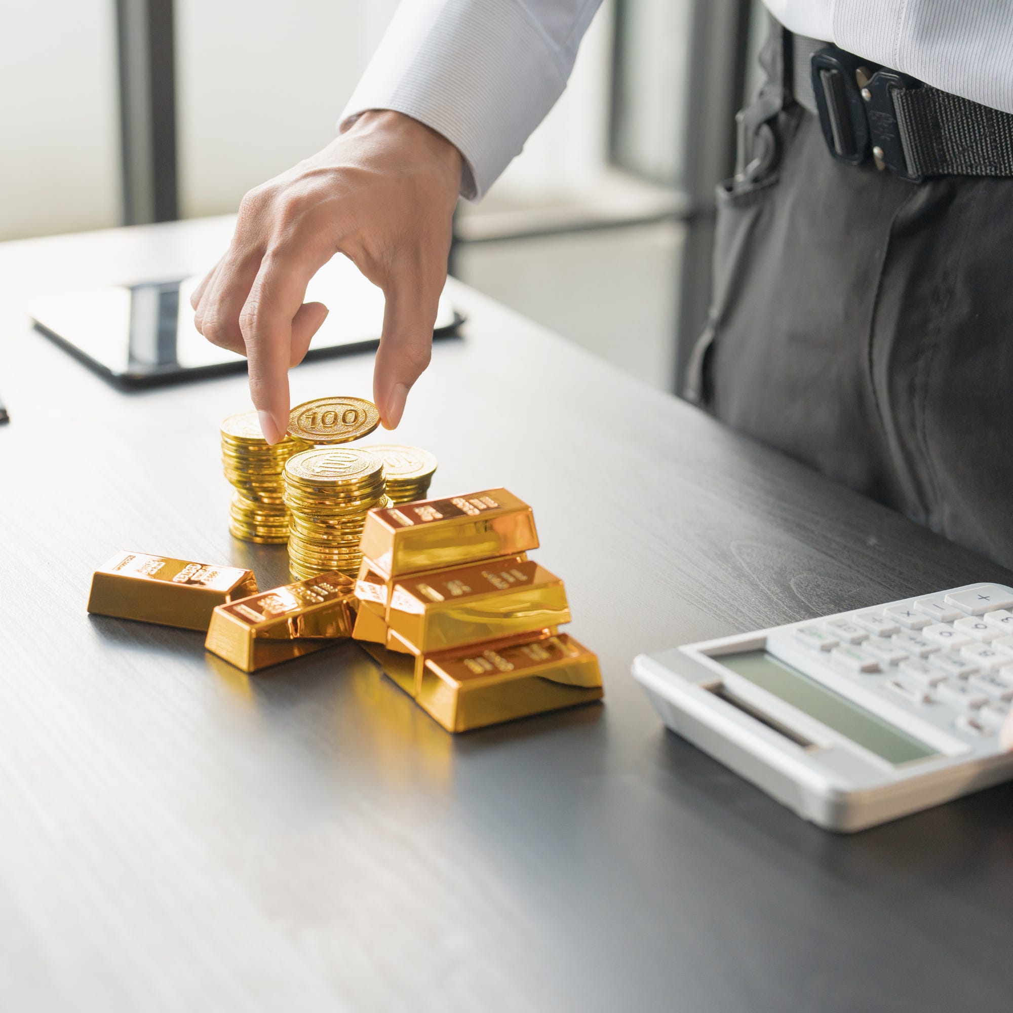 Hand bij goudstaven, munten en een rekenmachine als metafoor voor waarde, tijd, arbeid en financiële macht. Hand bij goudstaven, munten en een rekenmachine als metafoor voor waarde, tijd, arbeid en financiële macht.