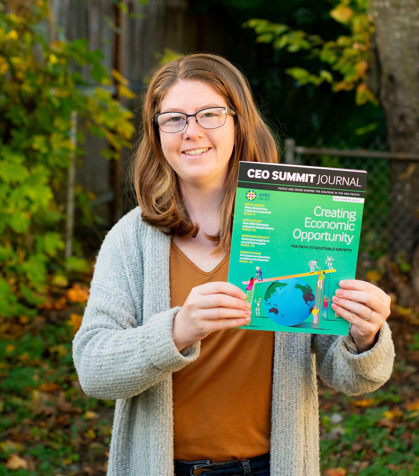 Me, a white woman with red hair, holding the journal outside with trees and fallen leaves in the background. Me, a white woman with red hair, holding the journal outside with trees and fallen leaves in the background.