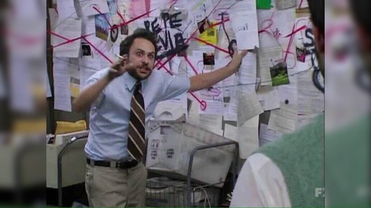 Charlie Day, the actor who plays Charlie Kelly in It's Always Sunny In Philadelphia, stands in front of a wall covered in papers with red lines drawn all over them. He holds a cigarette and gestures at the wall. His eyes brim with madness. 