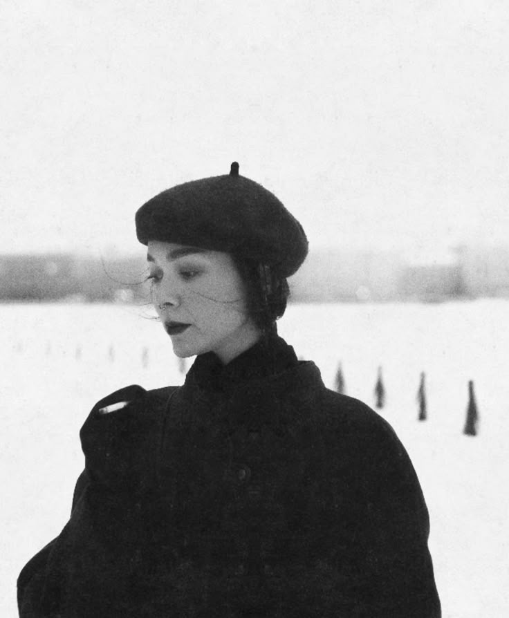 This may contain: black and white photograph of a woman in the snow wearing a hat with ear muffs