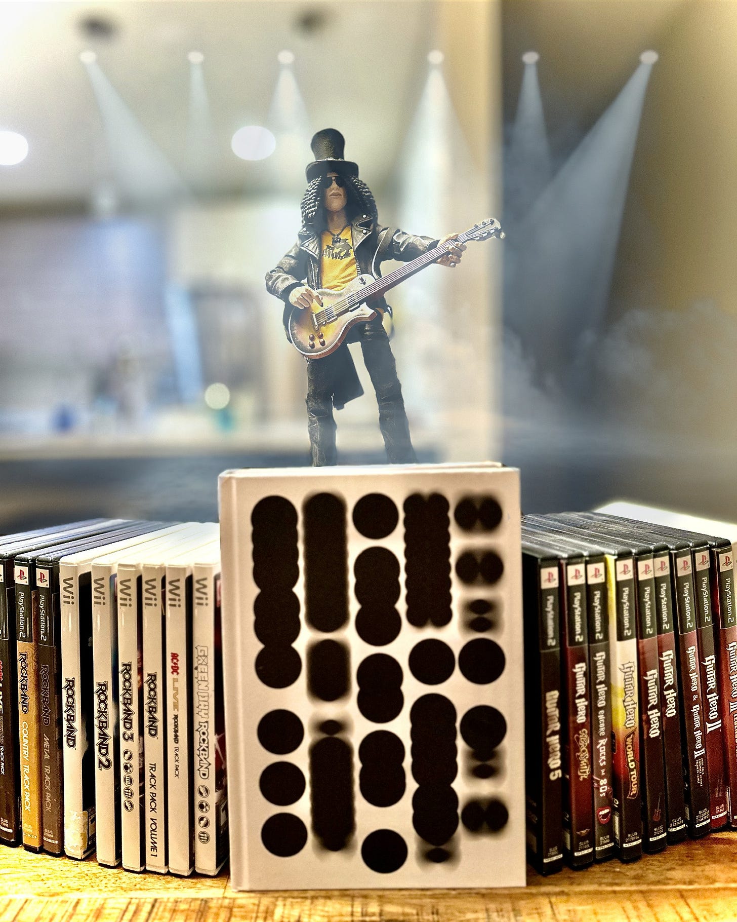 The cover of The Oral History of Guitar Hero, Rock Band and the Music Game Boom surrounded by games and standing atop is Slash playing Guitar. The cover of The Oral History of Guitar Hero, Rock Band and the Music Game Boom surrounded by games and standing atop is Slash playing Guitar.