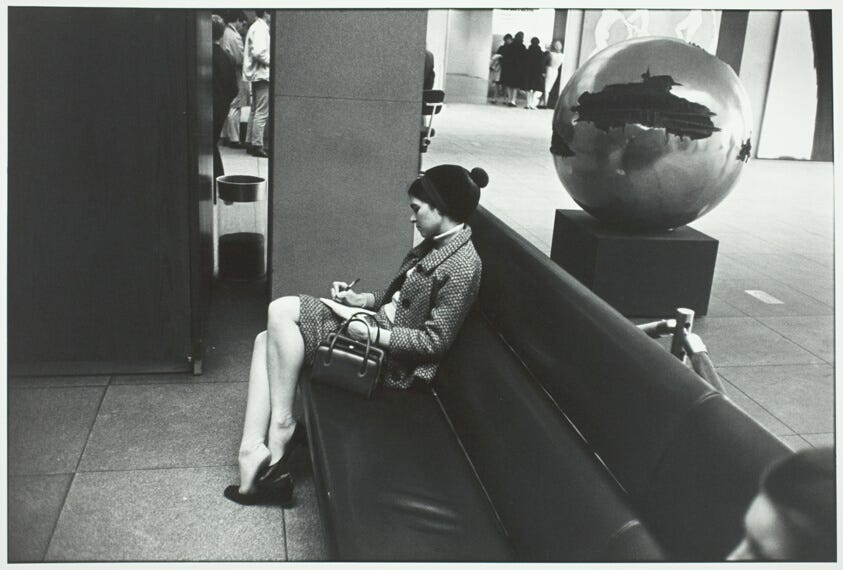 Black-and-white photo of woman sitting on a bench writing in a notebook. Behind her is a spherical reflective sculpture. Black-and-white photo of woman sitting on a bench writing in a notebook. Behind her is a spherical reflective sculpture.