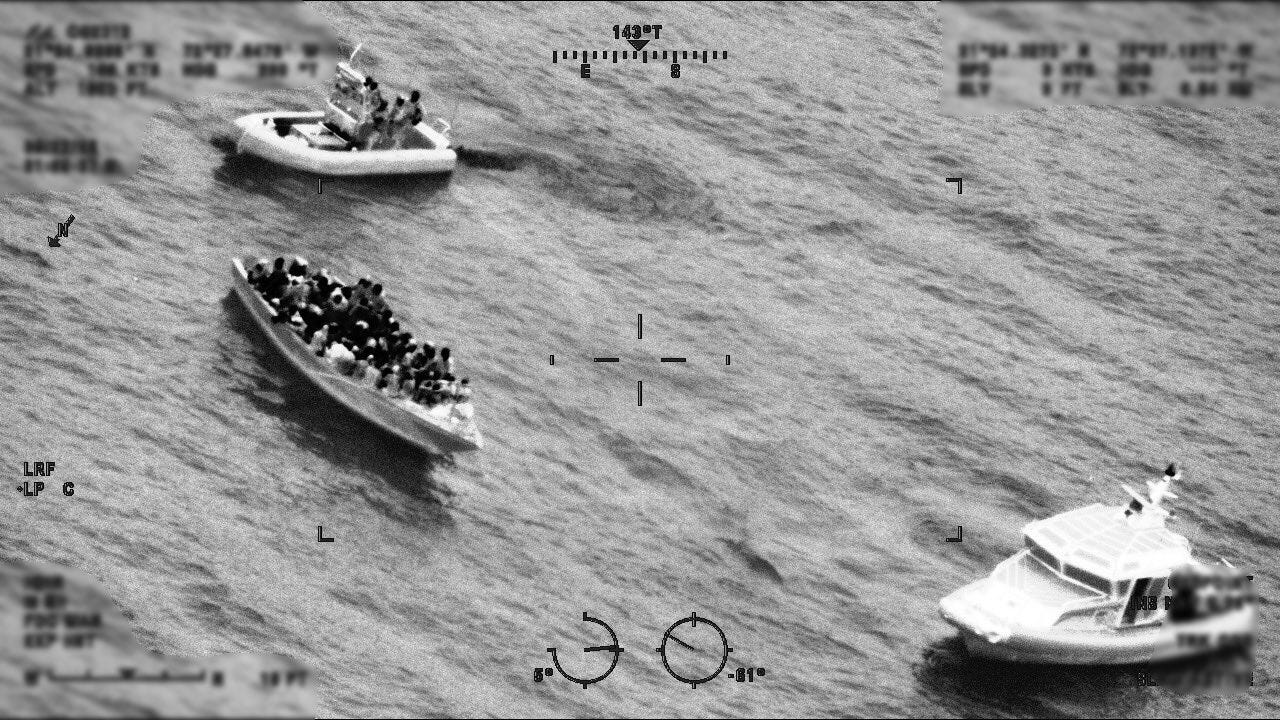 A US Coast Guard boarding party approaches a dangerously overloaded boat packed with Haitians as a Turks & Caicos Police Boat stands watch. A US Coast Guard boarding party approaches a dangerously overloaded boat packed with Haitians as a Turks & Caicos Police Boat stands watch.