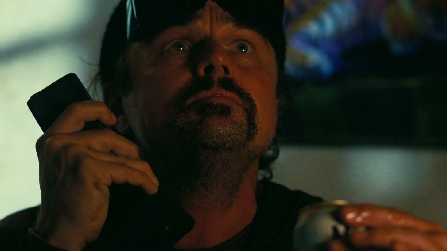 Bob, with sunglasses on his forehead, holds a phone in one hand and a beer can in the other, looking up