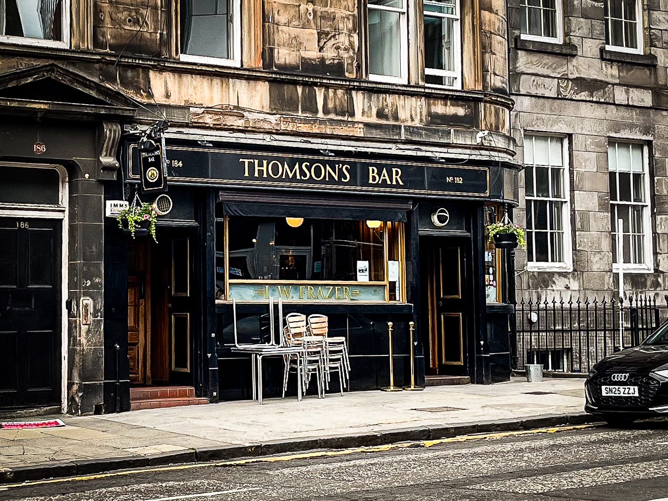 A simple black exterior of a pub. The sign, Thomson's Bar, is in gold serif font.