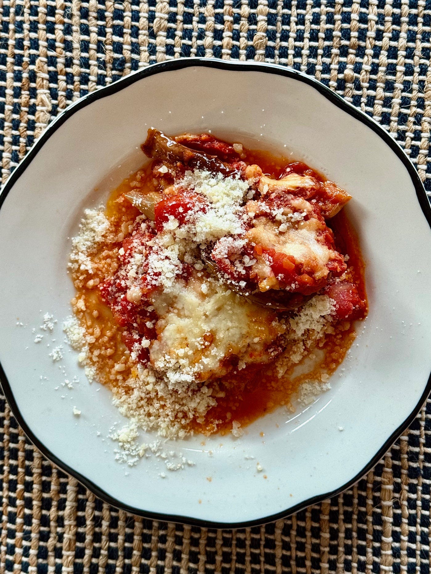 A white plate with eggplant parmesan on it. 
