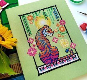 A gorgeous cross stitch of a resting tiger with her back to us.  Her body colorings and stripes are a gradient of deep oranges and blues.  There are many details, like hanging vines, florals, and a butterly sampler band at the bottom. 