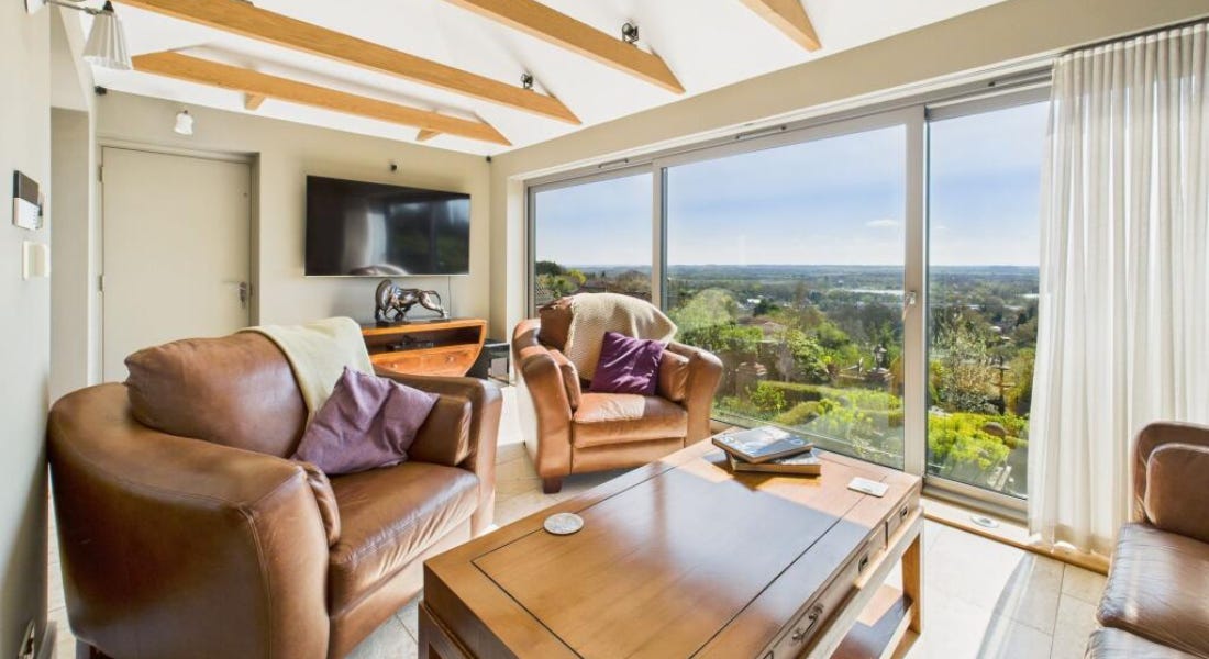 A living room with brown armchairs, a coffee table, a ceiling with wooden beams, and a window with a countryside view A living room with brown armchairs, a coffee table, a ceiling with wooden beams, and a window with a countryside view
