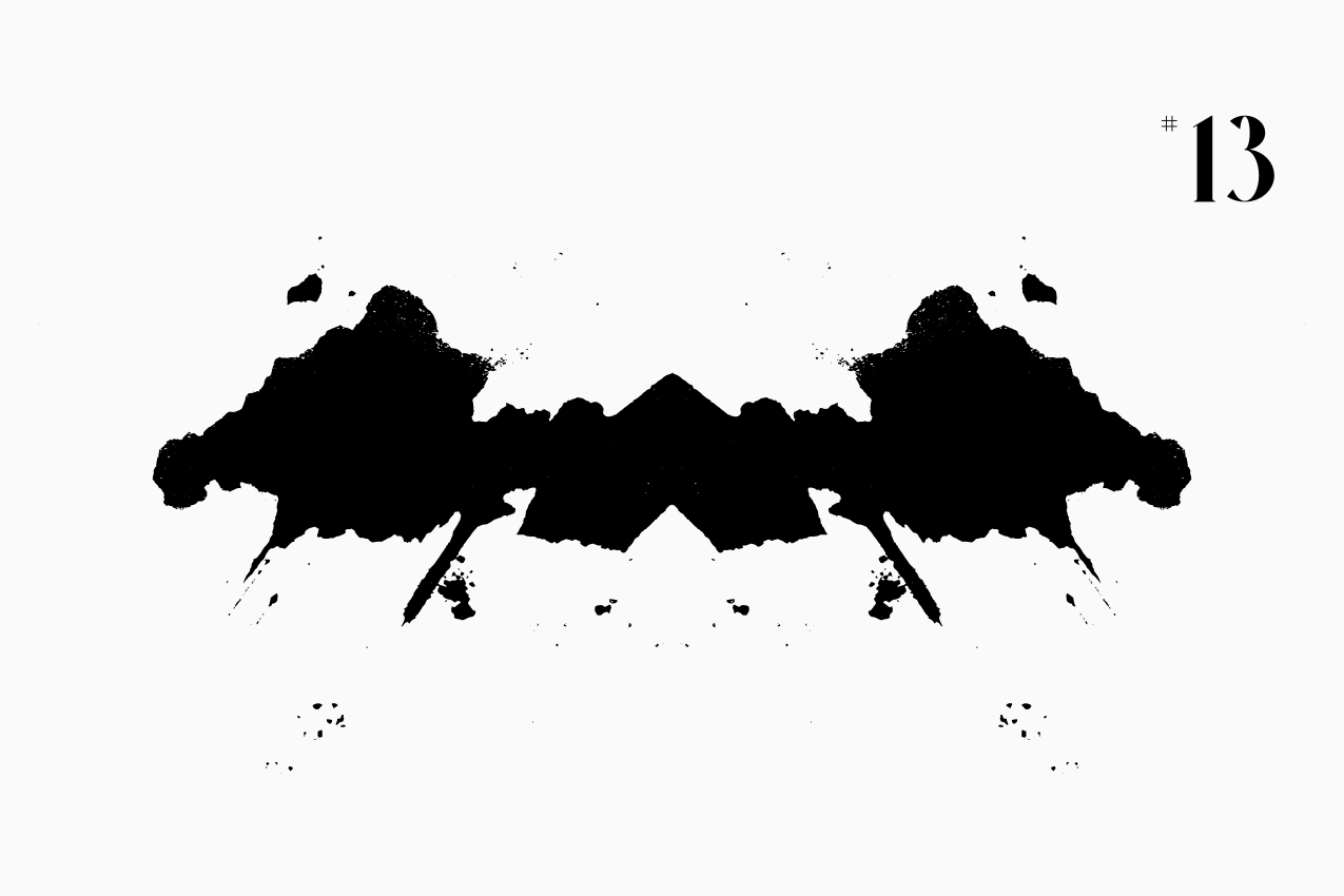 A bilateral, Rorschach-style inkblot specimen for the “In Other Words” series from The Subtext Review. The charcoal-black symmetrical splatter is centered on a cream paper background, labeled as Puzzle No. 13 in a classic serif typeface.
