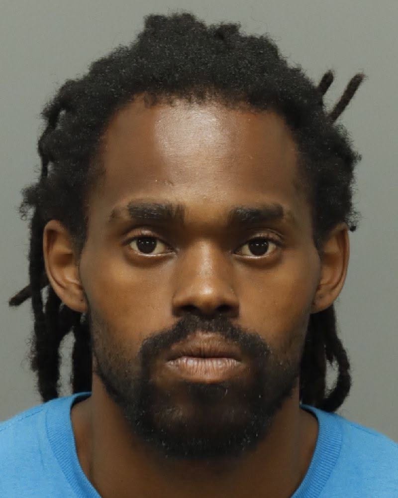 Mugshot of Christopher Key-Torrion Carnes, a 33-year-old Black man with dreadlocks, a beard, and wearing a blue shirt.