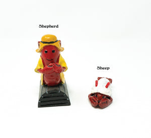 a lobster replica dressed in the traditional yellow slicker of fishermen everywhere standing on top of a lobster trap. He is labeled “Shepherd.” Next to him is a smaller lobster lying on the ground with what looks like a fleece blanket on top of him. He is labeled “sheep.”