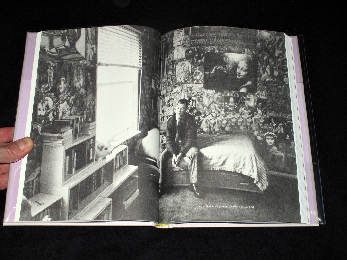 b/w photo of Orton sitting on a bed in front of a wall decorated with artworks cut out of books. The image appears as a double page spread in a book