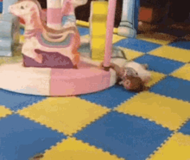 a child is laying on the floor in front of a carousel . a child is laying on the floor in front of a carousel .