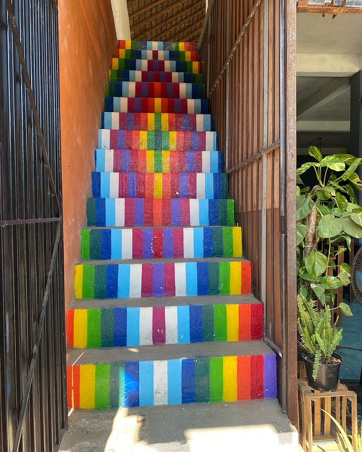 A multicolored rainbow staircase leads to restaurants on the main promenade of Zipolite. Palm trees and a white washed bell tower brush the clear blue skies from the vista of Hotel Punta del Sol