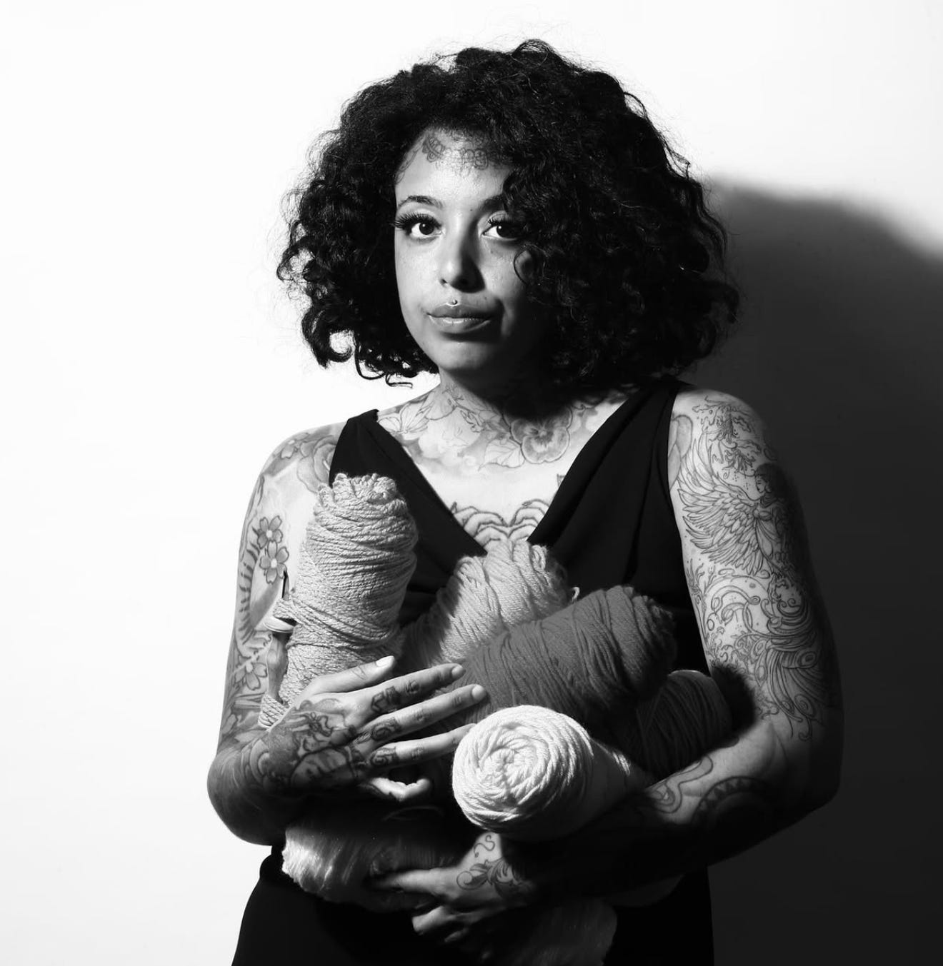 Honey Pierre in a black dress holding several large skeins of yarn against a white backdrop.