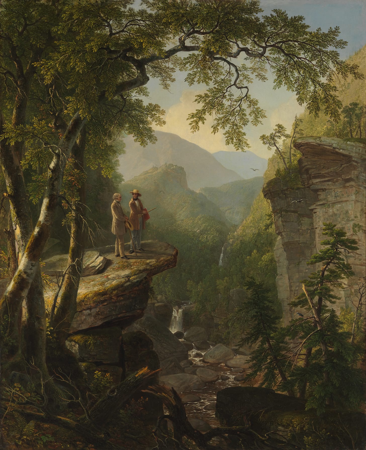 Two figures stand on a rocky ledge in a wooded gorge above a small waterfall Two figures stand on a rocky ledge in a wooded gorge above a small waterfall