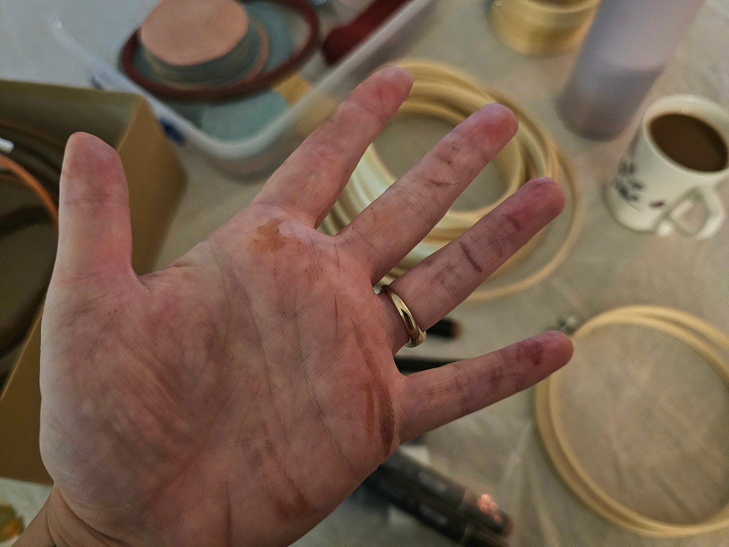 close-up of a hand covered in marker streaks held against a background of scattered embroidery supplies and a cup of coffee close-up of a hand covered in marker streaks held against a background of scattered embroidery supplies and a cup of coffee
