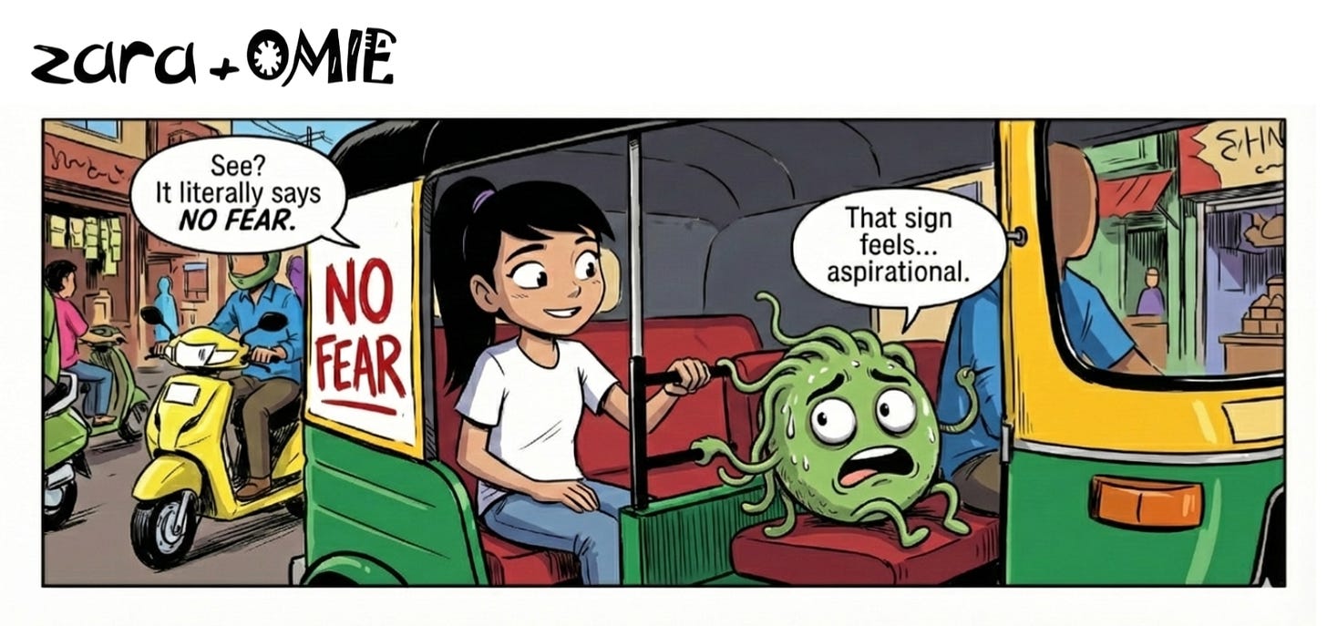 Zara and Omie sit in a moving auto rickshaw in India beneath a “NO FEAR” sign; Zara looks calm while Omie looks nervous.