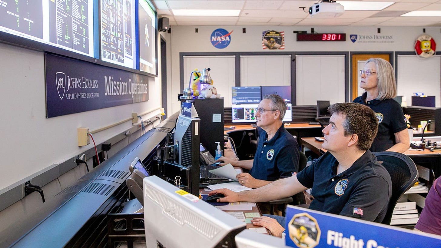 Flight operators at computers in a mission control center monitor spacecraft data on large wall displays. Flight operators at computers in a mission control center monitor spacecraft data on large wall displays.
