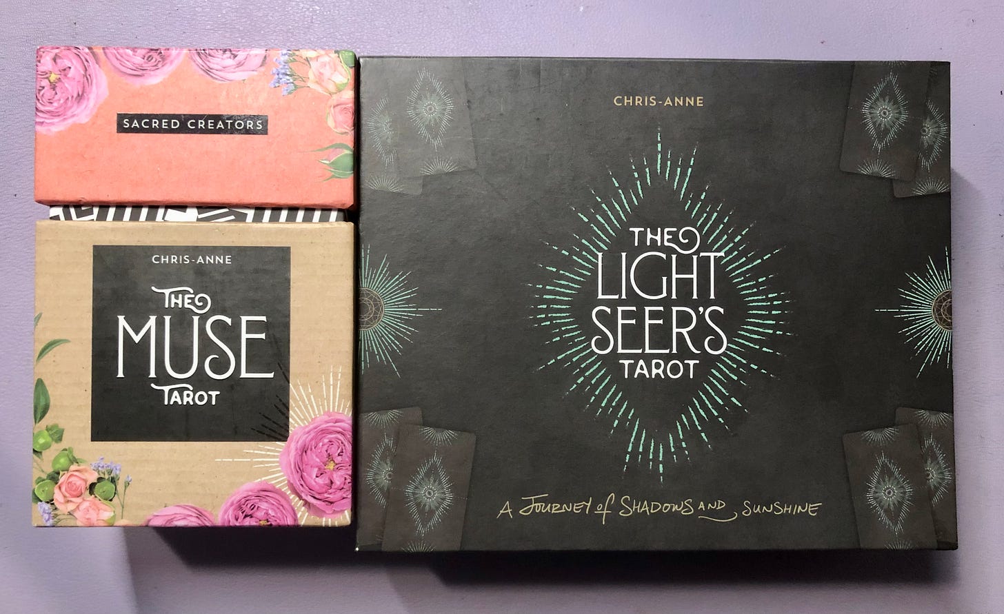 Two tarot deck boxes by Chris-Anne Donnelly: The Muse Tarot in a cream-coloured box with floral design and black label, and The Light Seer's Tarot in a dark box with radiating light design and the subtitle 'A Journey of Shadows and Sunshine'.