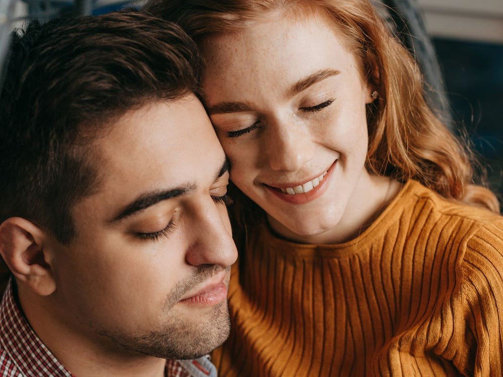 A young dark haired man and a red haired woman sitting close