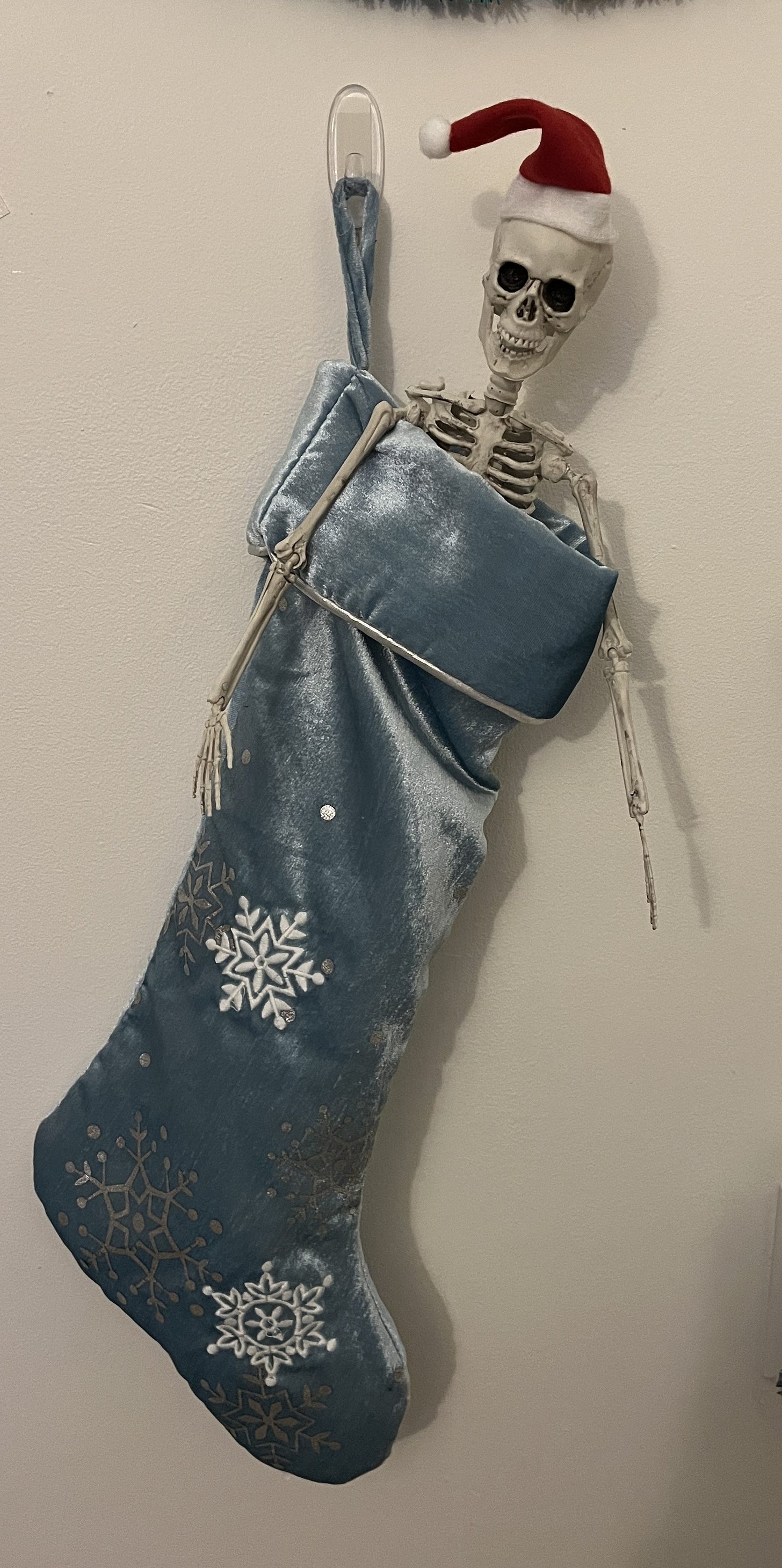 A toy skeleton wearing a Santa hat and sitting inside a Christmas stocking hanging from the wall.