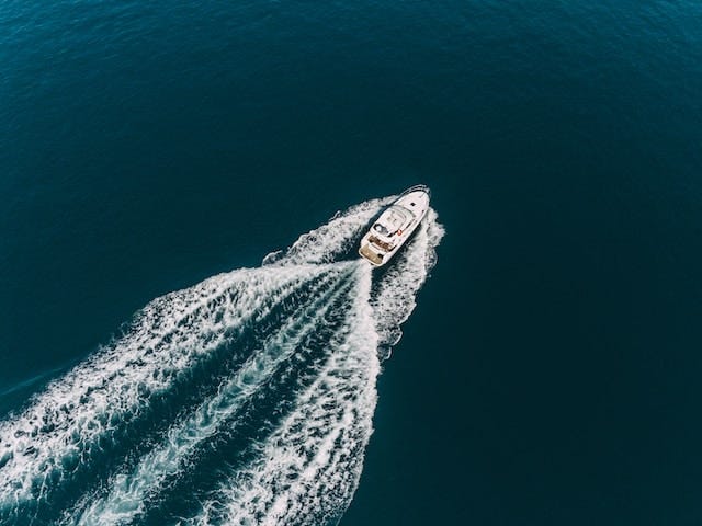 An overhead photograph of a luxury yacht sailing across the ocean, with a large wake behind it.