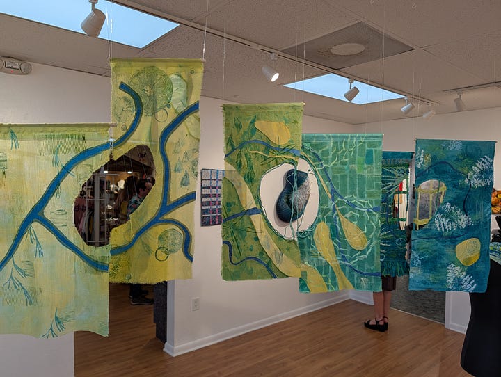 Image on the left shows six pieces of paper with diagrams on them. Image on the right shows six panels of fabric with similar diagrams, framing a view of a work of art on the far wall.
