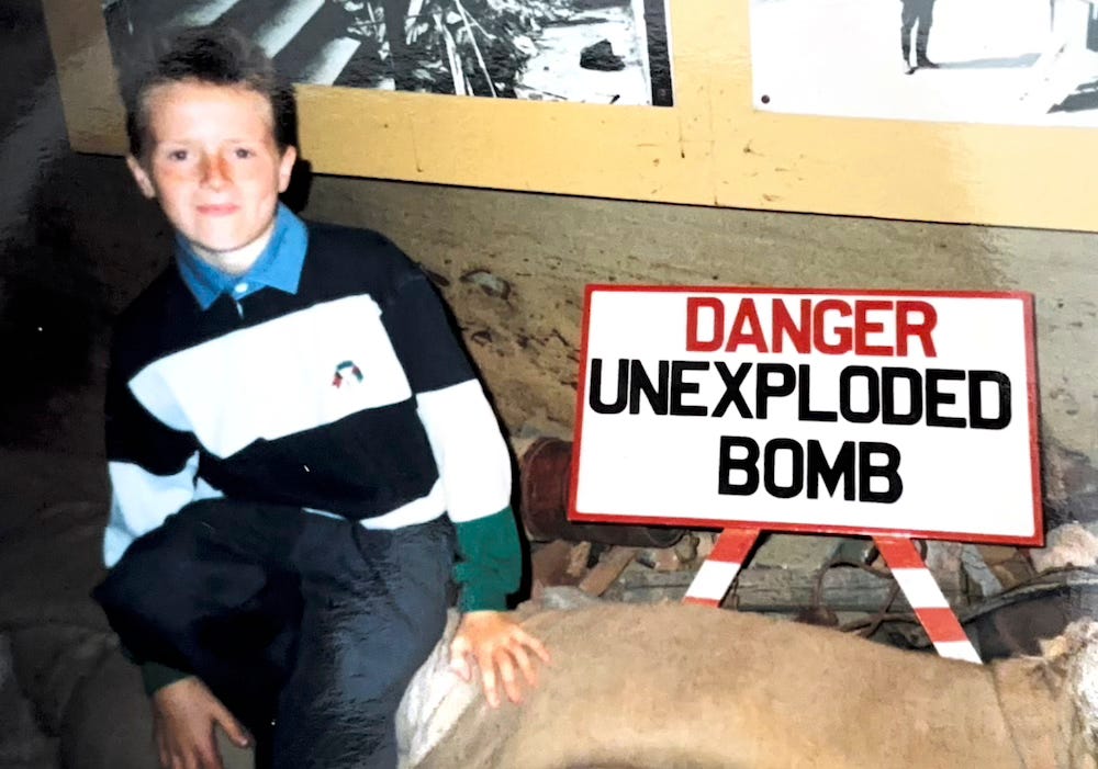 Me at about 12 years old, sitting in a museum on sandbags, next to a sign that says 'danger, unexploded bmb'