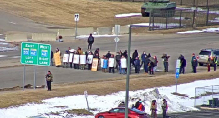 Telephoto lens picture of maybe 20 protesters standing across a road while holding homemade shields. Telephoto lens picture of maybe 20 protesters standing across a road while holding homemade shields.