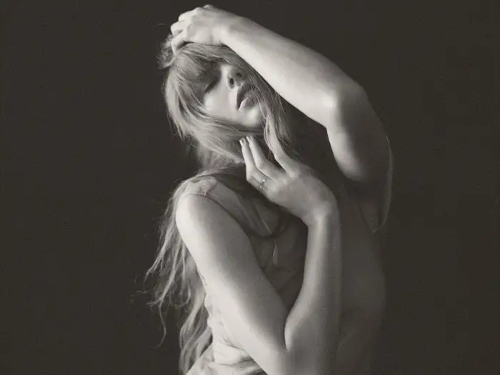 Taylor Swift in a black and white photograph where she is cradling her head in a sexy but tortuous way.