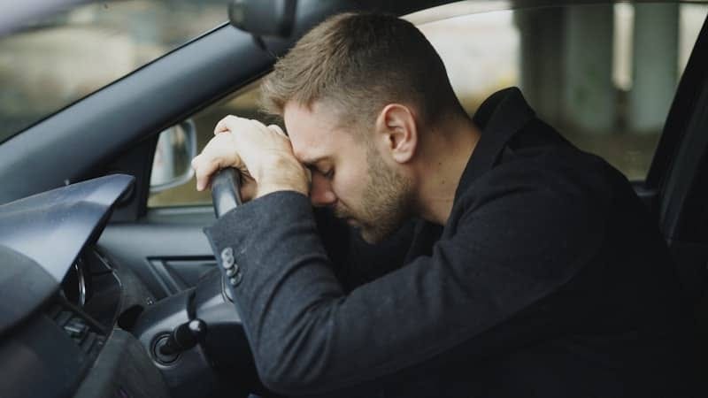 Man resting head on steering wheel in car.