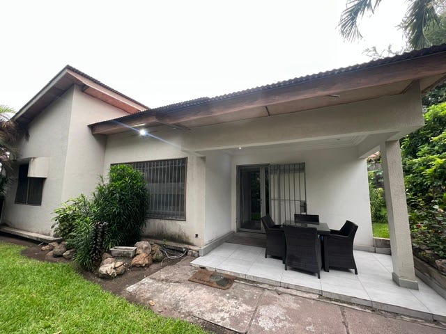 A white-washed stucco home with dark metal bars on the windows and a paved walkway leading between a house and a garden