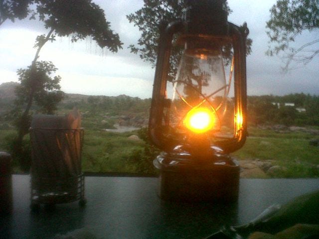 A lantern burns in the foreground. In the background there are green fields and some trees. A lantern burns in the foreground. In the background there are green fields and some trees.