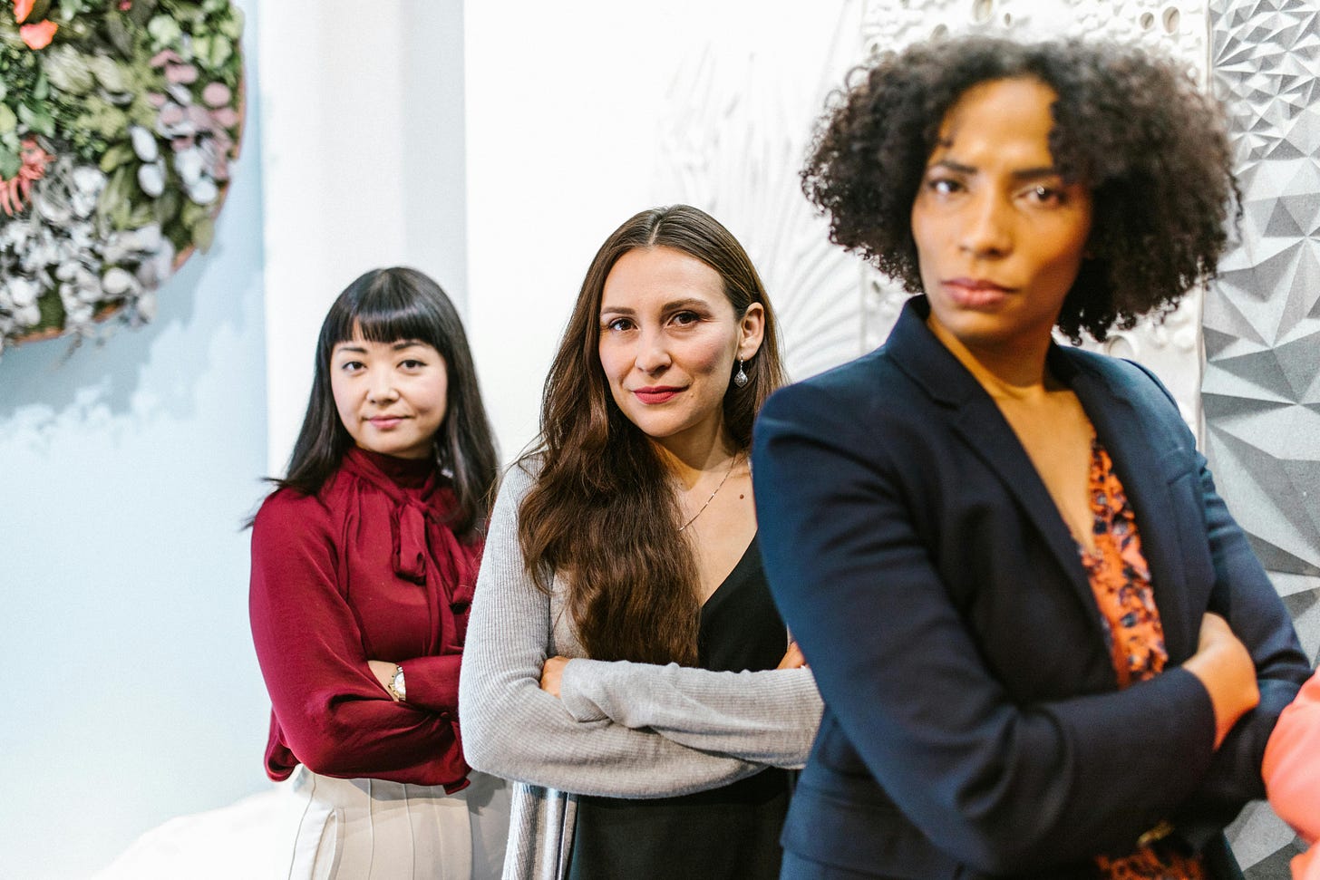 Three women at an office, wearing business clothes and crossing their arms over their chests