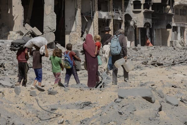 A row of Palestinians carrying some possessions and walking amid rubble in Gaza. 