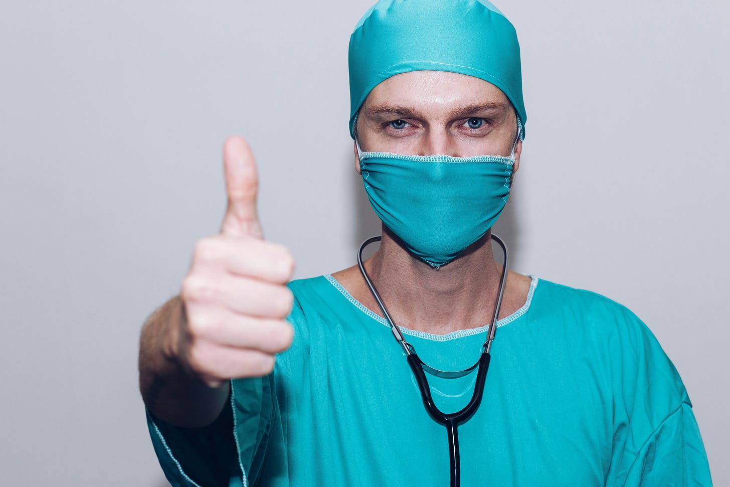 Medical professional in scrubs and wearing a stethoscope giving a thumbs up sign