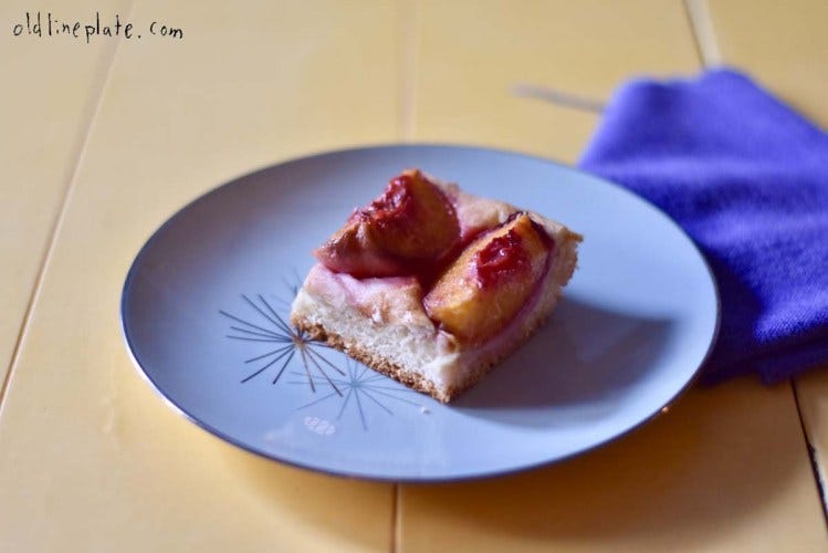 Slice of plum upside-down cake with caramelized fruit topping on blue plate with blue napkin on wooden table