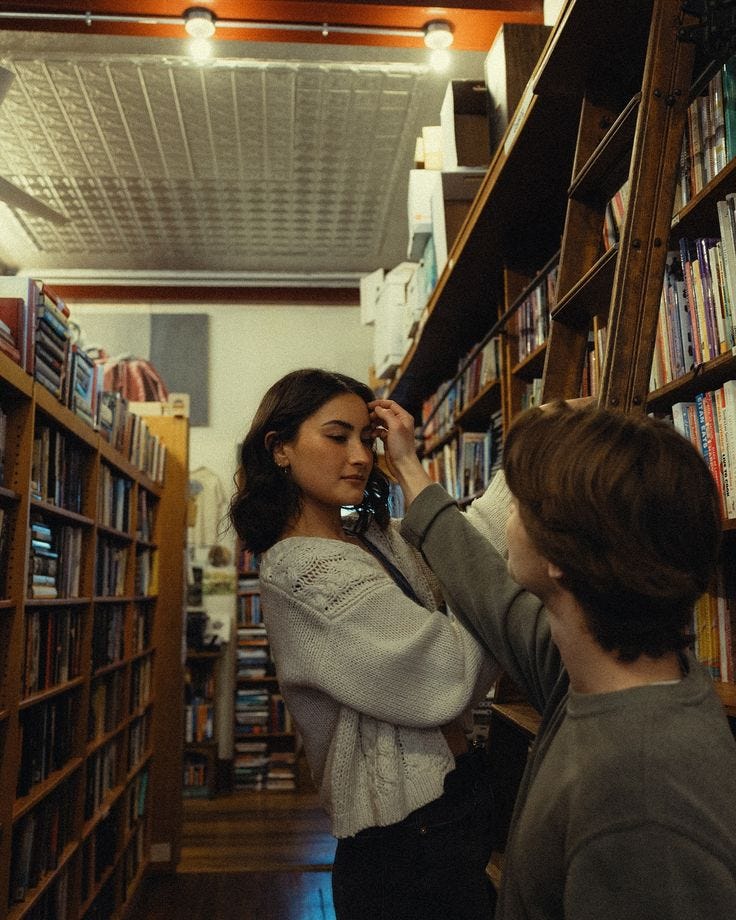 This may contain: two people standing in front of bookshelves talking on their cell phones and looking at them